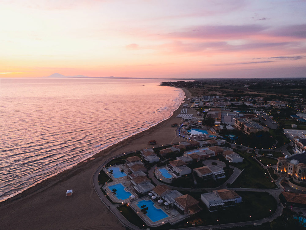 Aerial sunset view of the Aldemar Olympian Village beachfront resort, pools and coast.